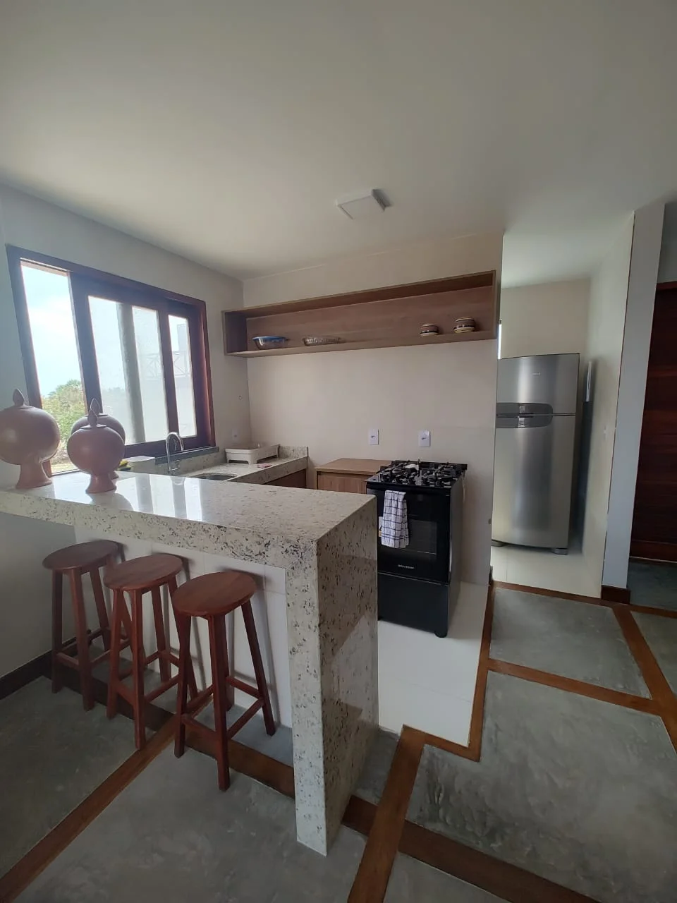 Cozinha iluminada com geladeira e bancada.